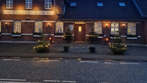 A brick building with a sign reading "Filsdorf Red" and multiple windows. There are small trees with lights in front.