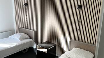 A hotel room with two single beds, a small bedside table, and a wall with vertical stripes.