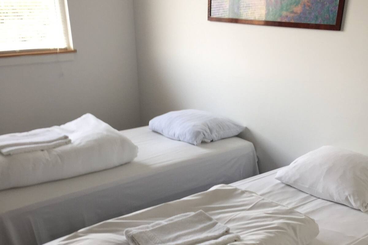 Quarto com duas camas de solteiro, cada uma com roupa de cama e almofadas brancas.