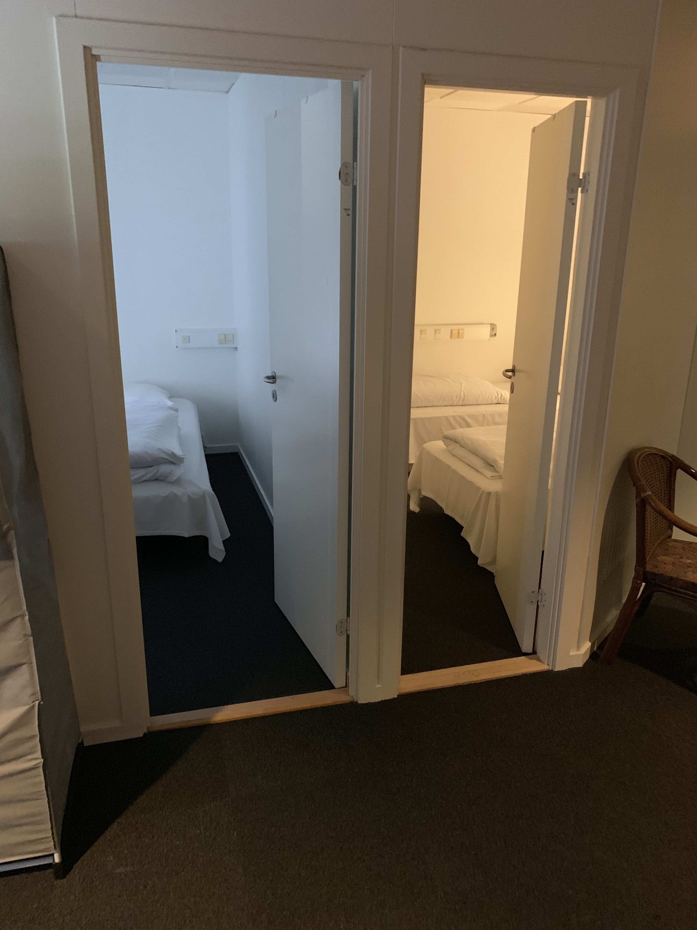 A hotel room with a bed, a chair, and a door leading to another room.