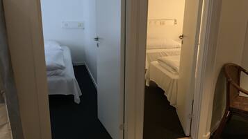 A hotel room with a bed, a chair, and a door leading to another room.
