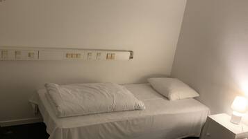 A hotel room with a single bed, a bedside table with a lamp, and a wall-mounted power outlet.
