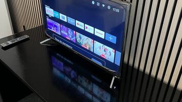 A flat-screen TV on a black stand with a remote control beside it, displaying a streaming service interface.