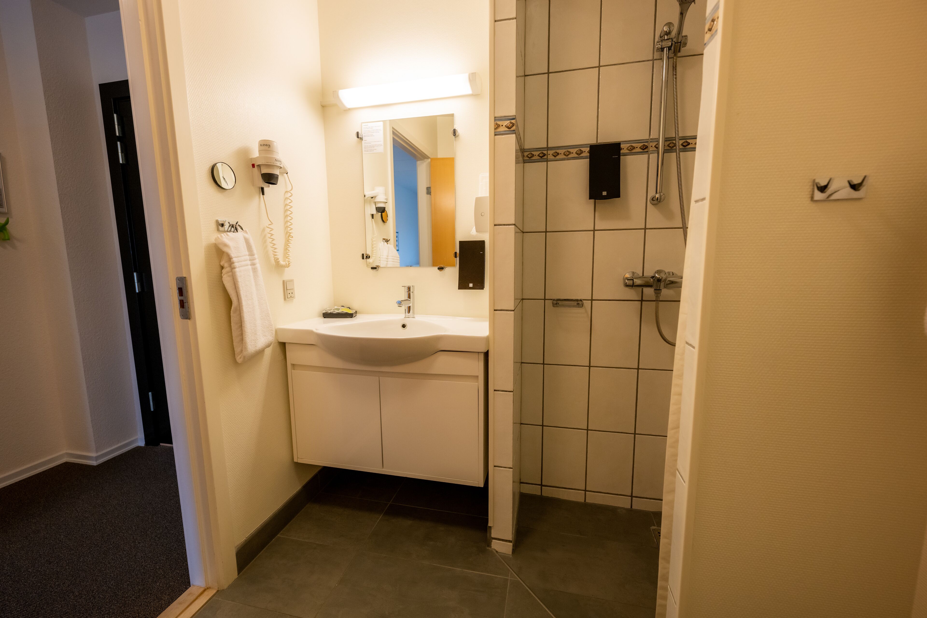 A bathroom with a sink, mirror, towel rack, and shower.