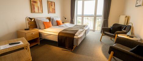 A hotel room with a bed, a desk, a chair, a small table, and a balcony with curtains.