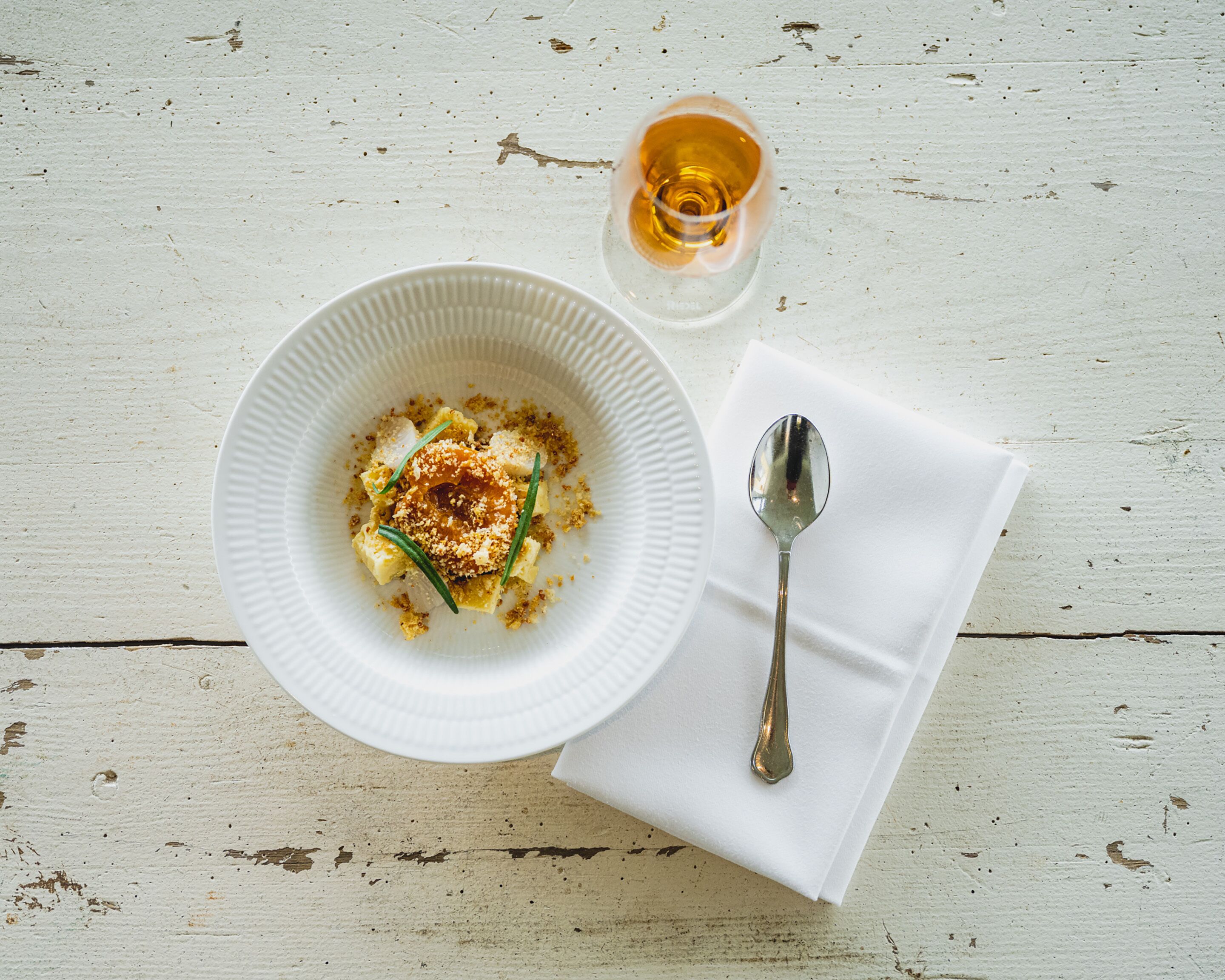 Un plato blanco con comida y una cuchara sobre un mantel blanco sobre una mesa de madera rústica.