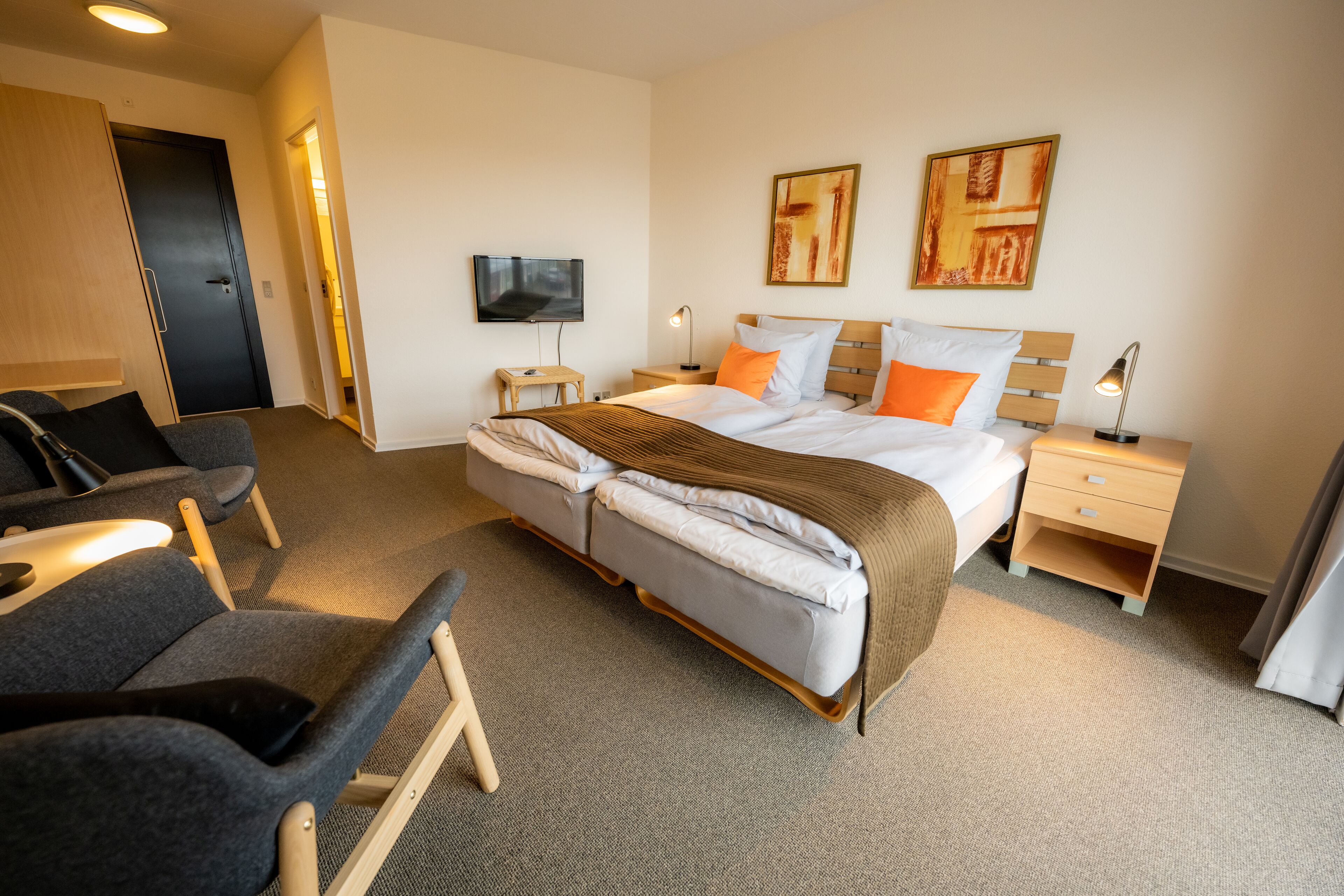A hotel room with a large bed, two bedside tables, a TV, and a seating area with chairs.