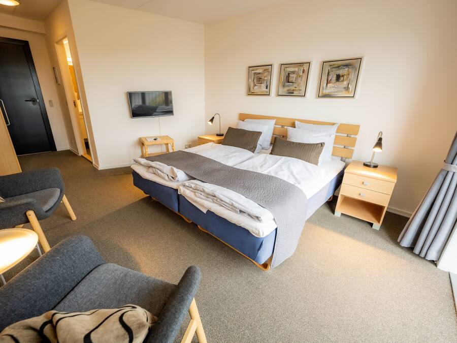 A hotel room with a bed, bedside tables, a TV, and artwork on the wall.