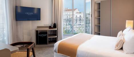 Una camera d'albergo con un letto, una scrivania, una TV e vista sui palazzi attraverso una finestra.