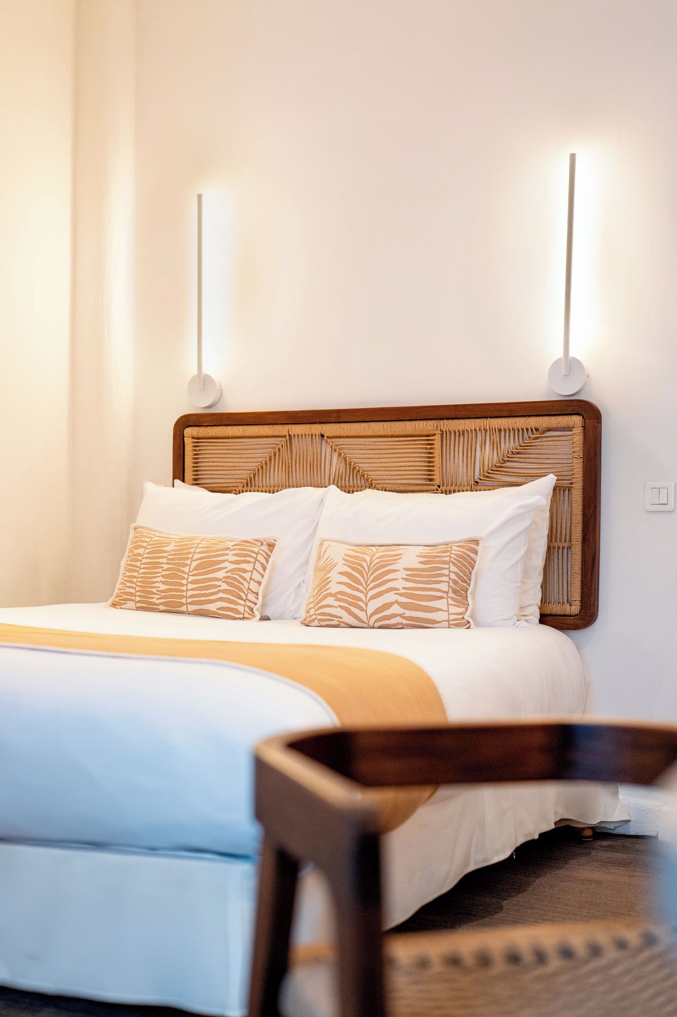 A neatly made bed with a wooden headboard, white bedding, and patterned pillows.