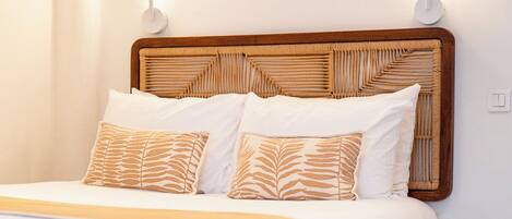 A neatly made bed with a wooden headboard, white bedding, and patterned pillows.