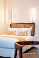 Una cama bien hecha con cabecera de madera, ropa de cama blanca y almohadas estampadas.