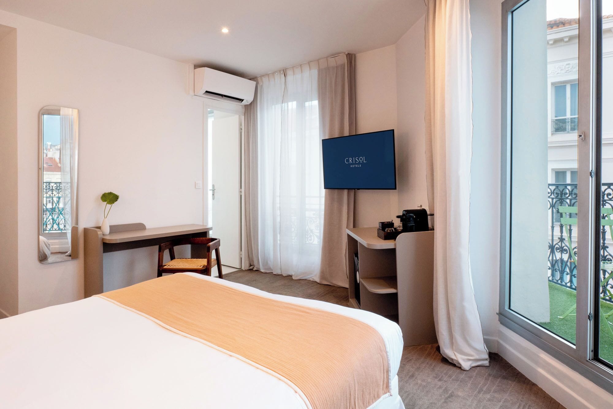 A hotel room with a bed, a desk, a chair, a TV, and a balcony with a view.