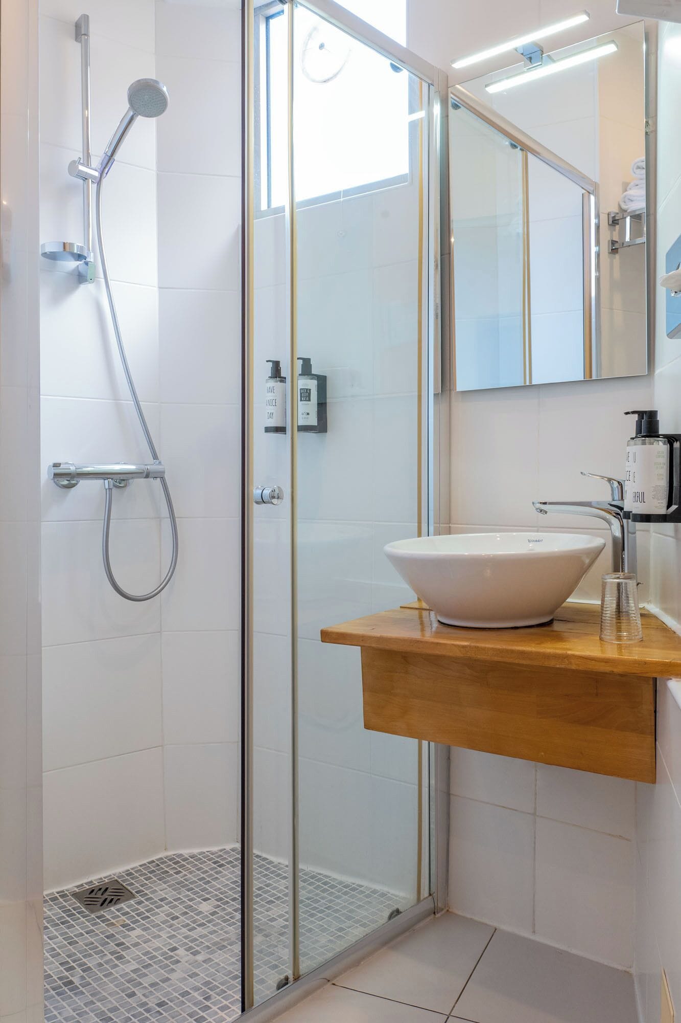 Une salle de bain moderne avec une douche à parois de verre, un lavabo blanc et un meuble-lavabo en bois.