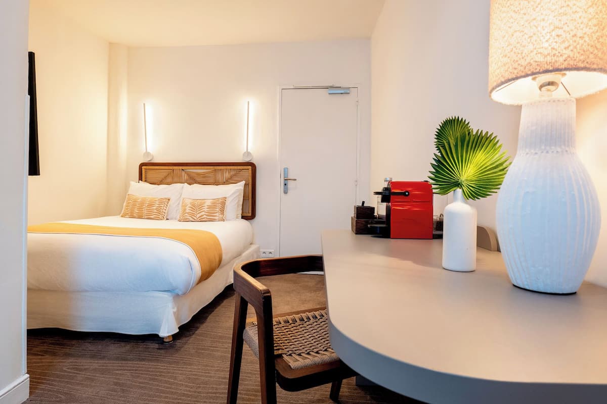 A hotel room with a bed, bedside table, lamp, and a door.
