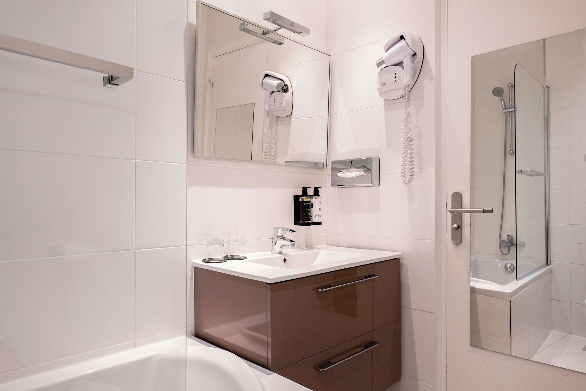 A modern bathroom with a bathtub, a shower, a vanity with a mirror, and a hairdryer mounted on the wall.