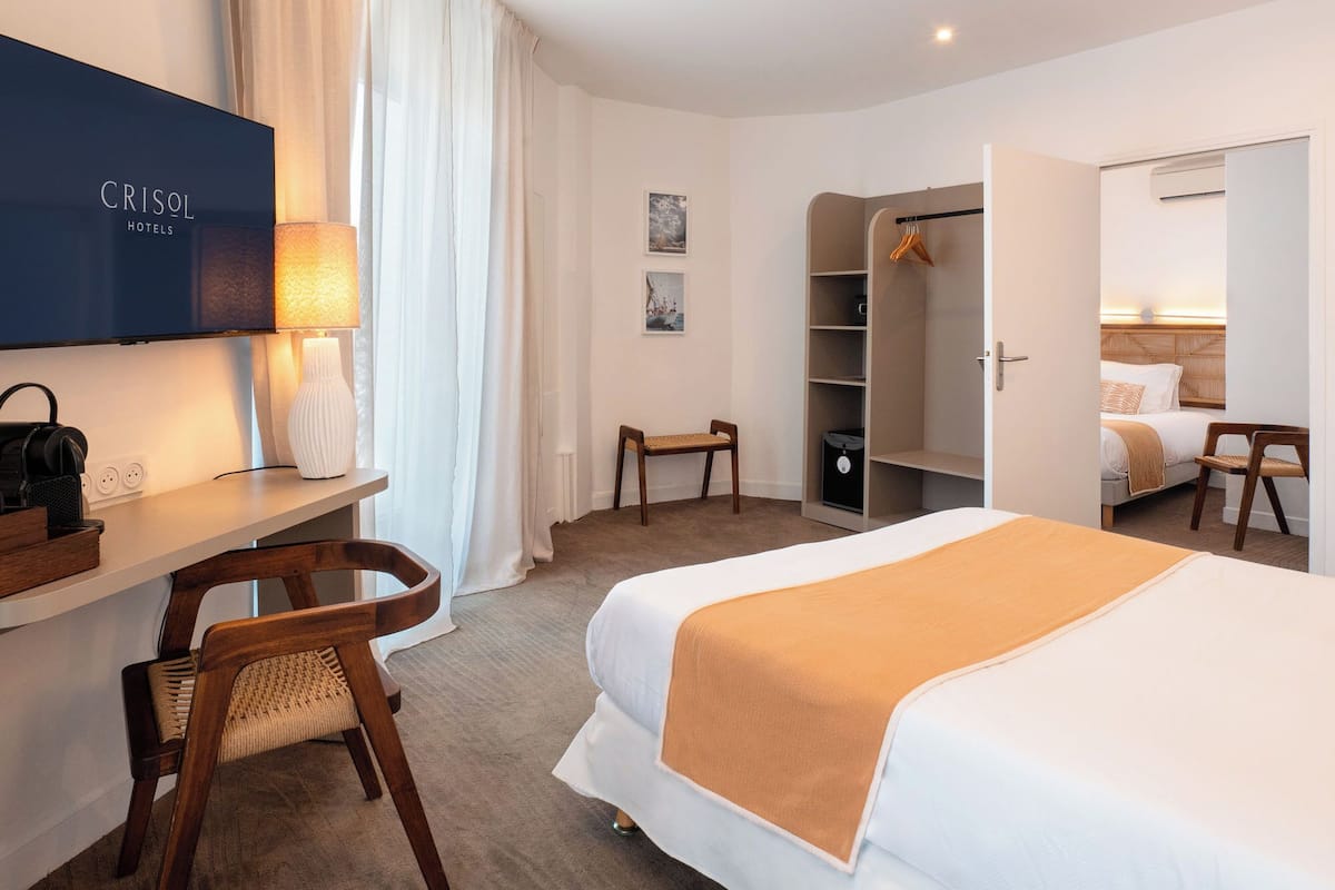 A hotel room with a bed, a desk with a lamp, a chair, a wardrobe, and a television.