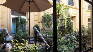 Un patio con zona de estar, una sombrilla grande y varias plantas en macetas.