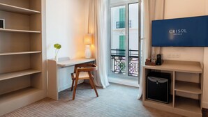 Habitación de hotel con escritorio, silla, televisión y estanterías.