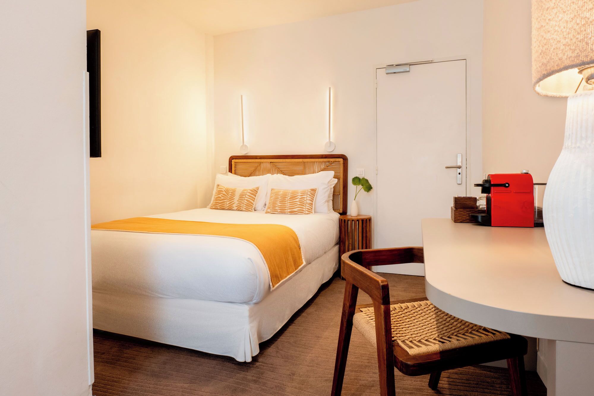 Una camera d'albergo con un letto, un comodino, una sedia e un tavolino con una lampada.
