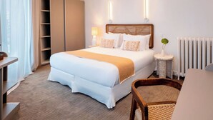 Una habitación de hotel con cama, mesitas de noche, una silla, un radiador y un armario.