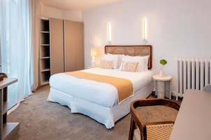 Quarto de hotel com cama, mesas de cabeceira, uma cadeira, radiador e guarda-roupa.