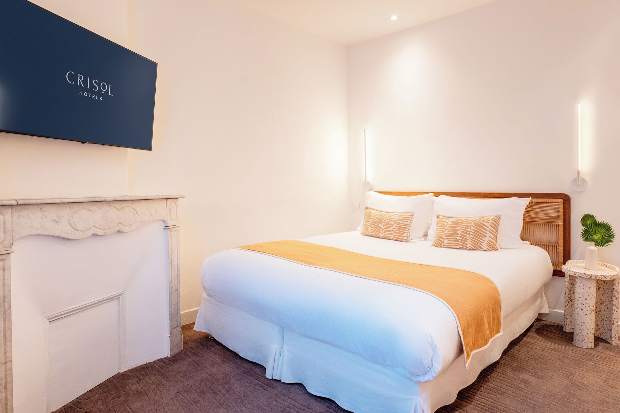 A hotel room with a bed, a nightstand, a wall-mounted TV, and a fireplace.
