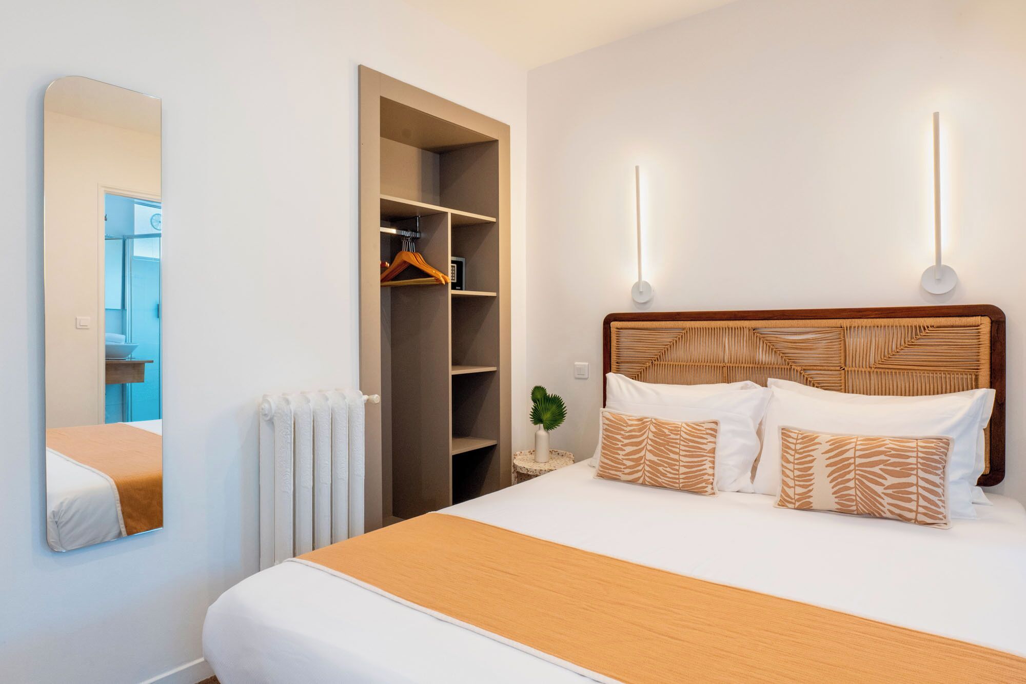 Habitación de hotel con cama, armario, espejo y mesita de noche con lámpara.