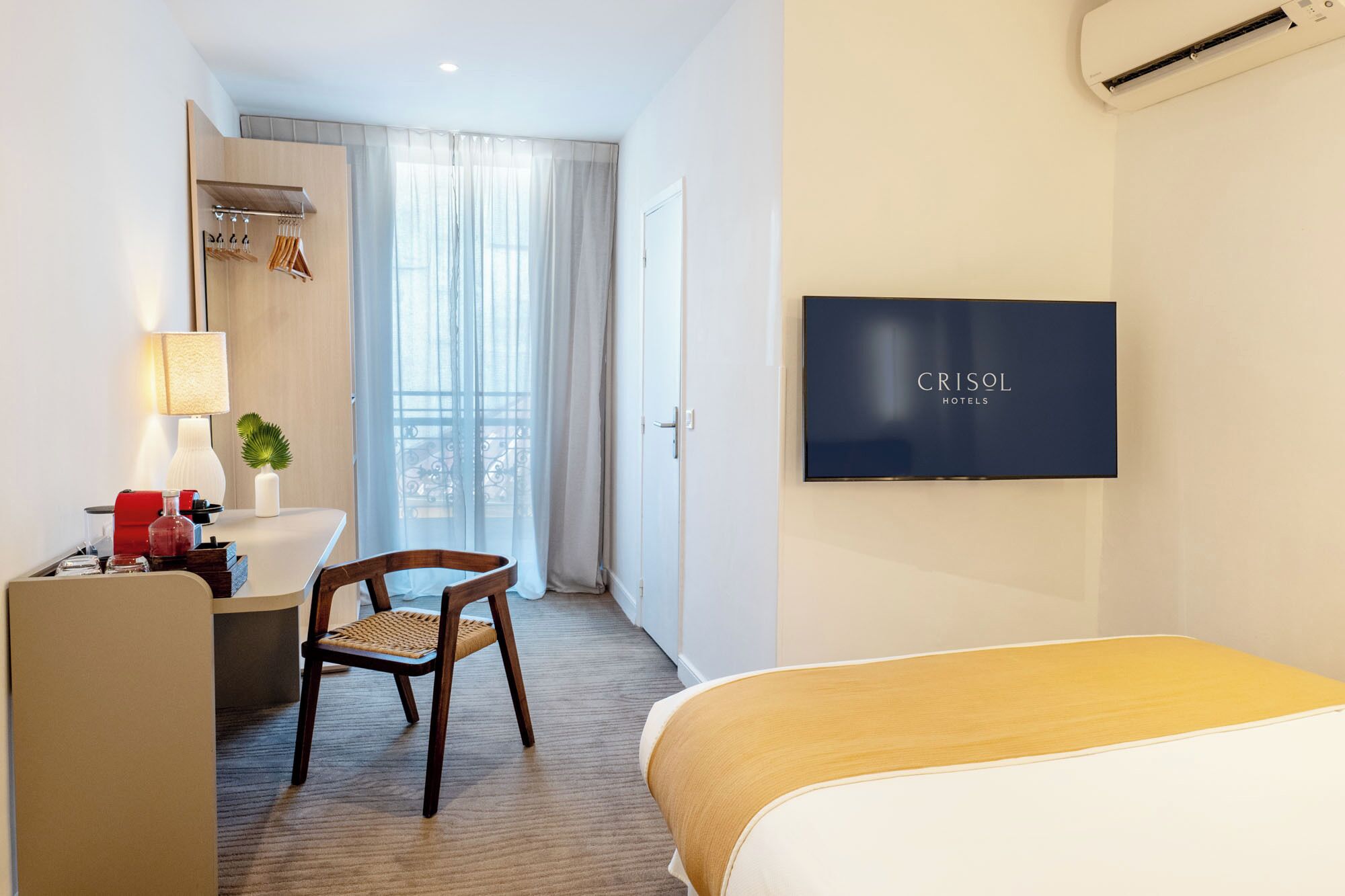Habitación de hotel con cama, escritorio con silla, televisión y baño con espejo y cortinas.