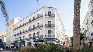 Un hotel de varios pisos con balcones, un restaurante a nivel de calle y una palmera en primer plano.