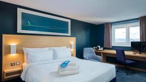 A hotel room with a large bed, a desk with a computer, a chair, and a window with curtains. - Travelodge York Central (York)