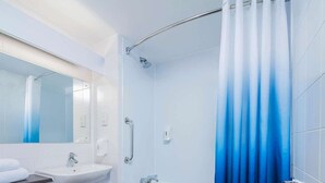 A modern bathroom with a white sink, a mirror, a shower with a blue gradient curtain, and a wooden floor. - Travelodge York Central (York)