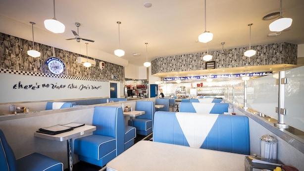 Un restaurant avec des banquettes bleues, un sol à carreaux et une horloge au mur.