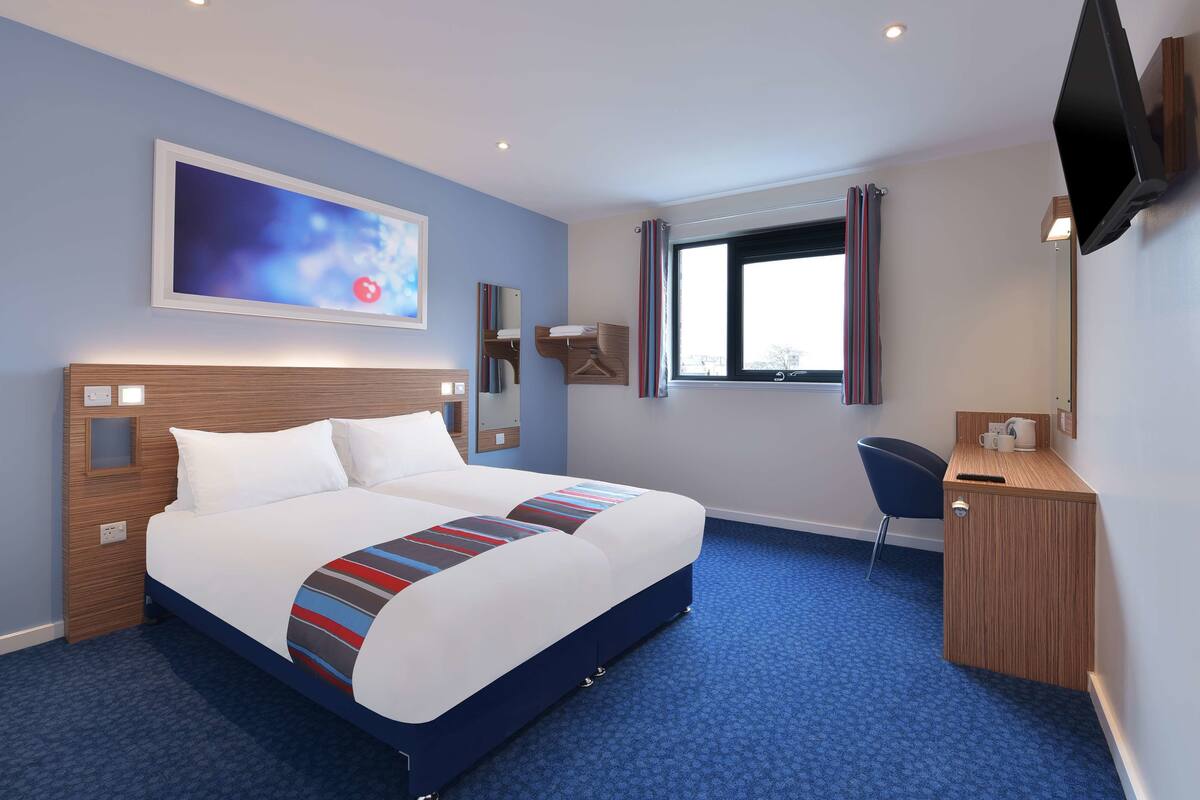A hotel room with a large bed, a desk, a chair, and a TV mounted on the wall.