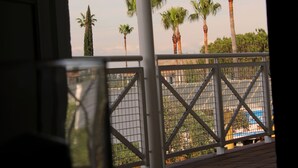 Een balkon met uitzicht op palmbomen en een gebouw op de achtergrond.
