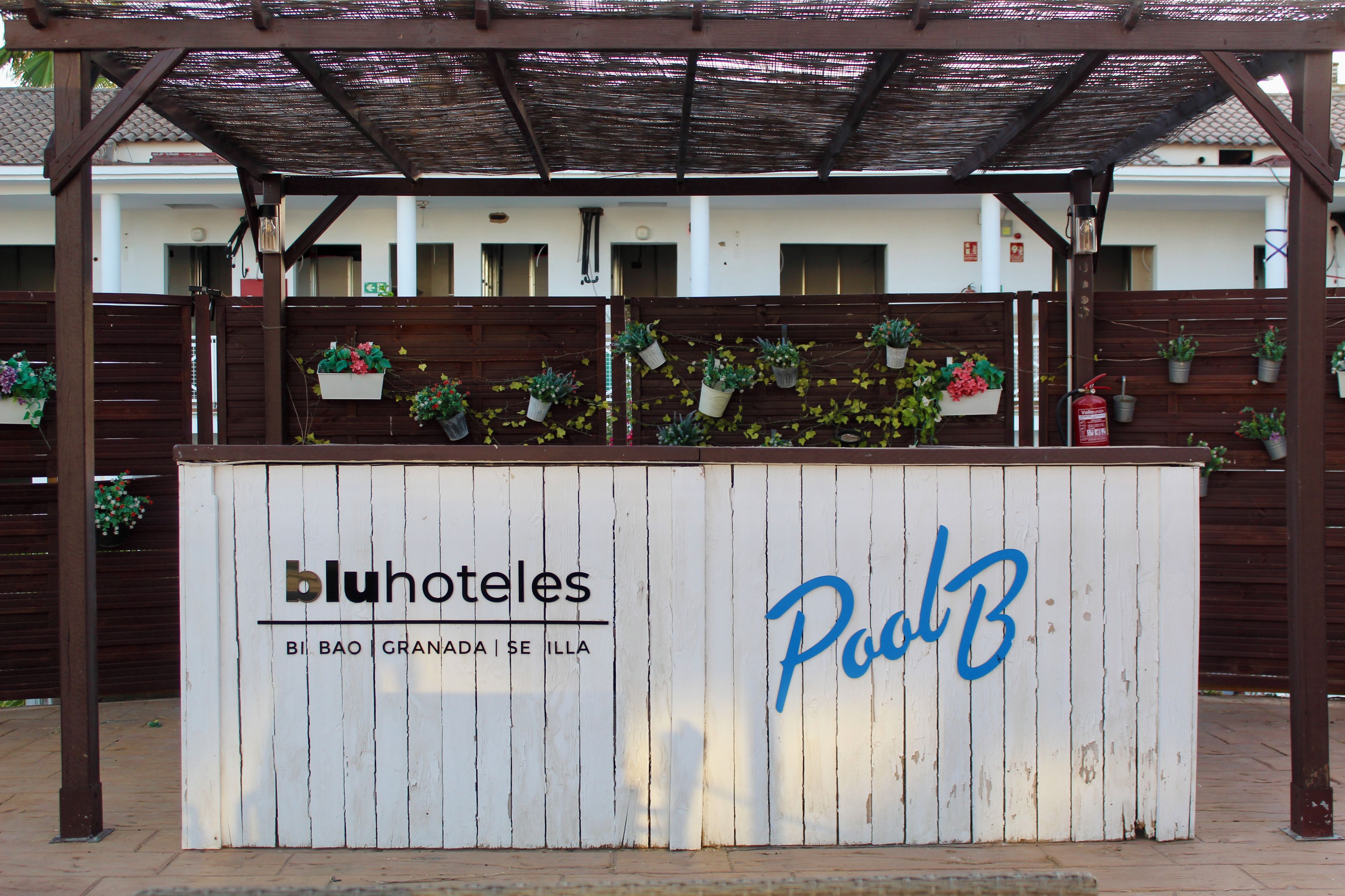 Entrada de un hotel con un letrero de madera que muestra el nombre 'bluhoteles' y 'Polo B' en letras azules.