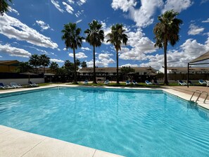 Une piscine avec des chaises longues et des palmiers.