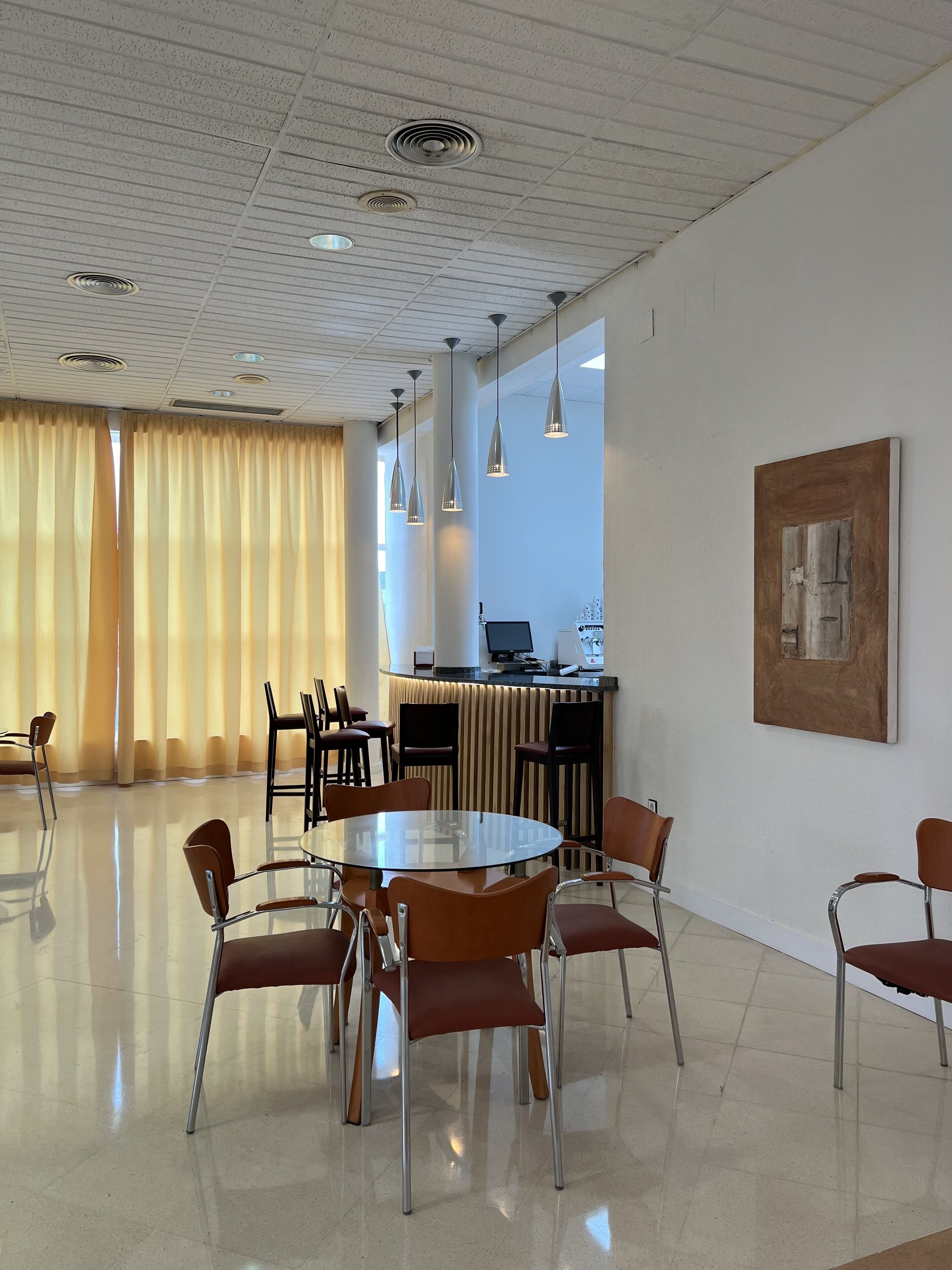Et moderne mødelokale med et rundt glasbord, flere stole, en receptionsdisk og et stort vindue med gardiner.