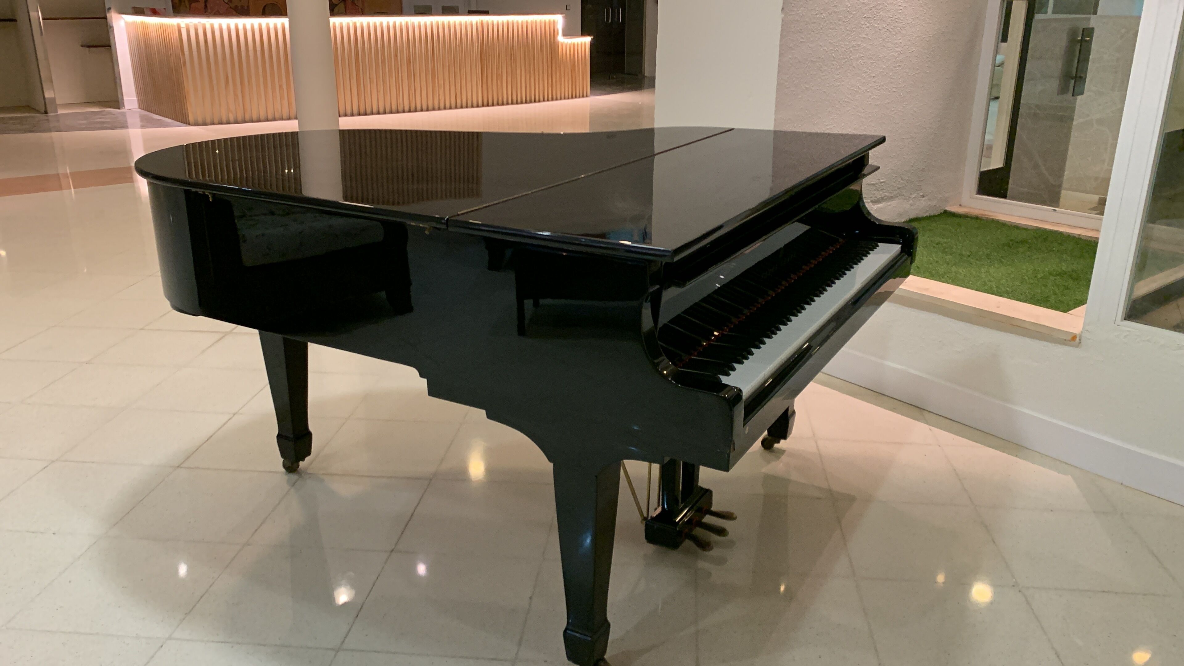 A black grand piano in a well-lit room with a tiled floor.