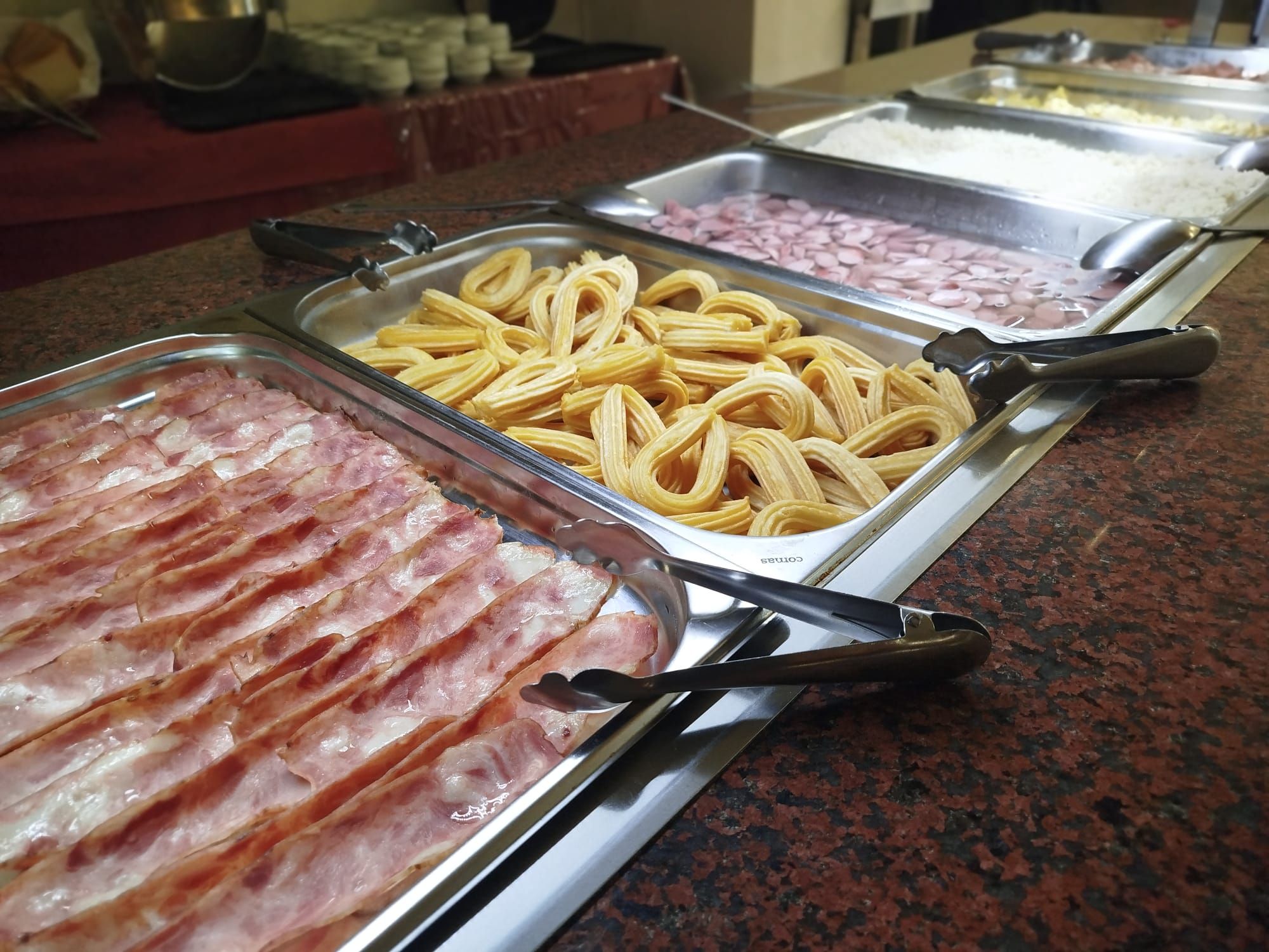 A buffet with various food items including bacon, pasta, and rice.