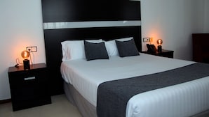 Une chambre à coucher moderne avec un grand lit, deux tables de chevet et une petite table de nuit avec une lampe.