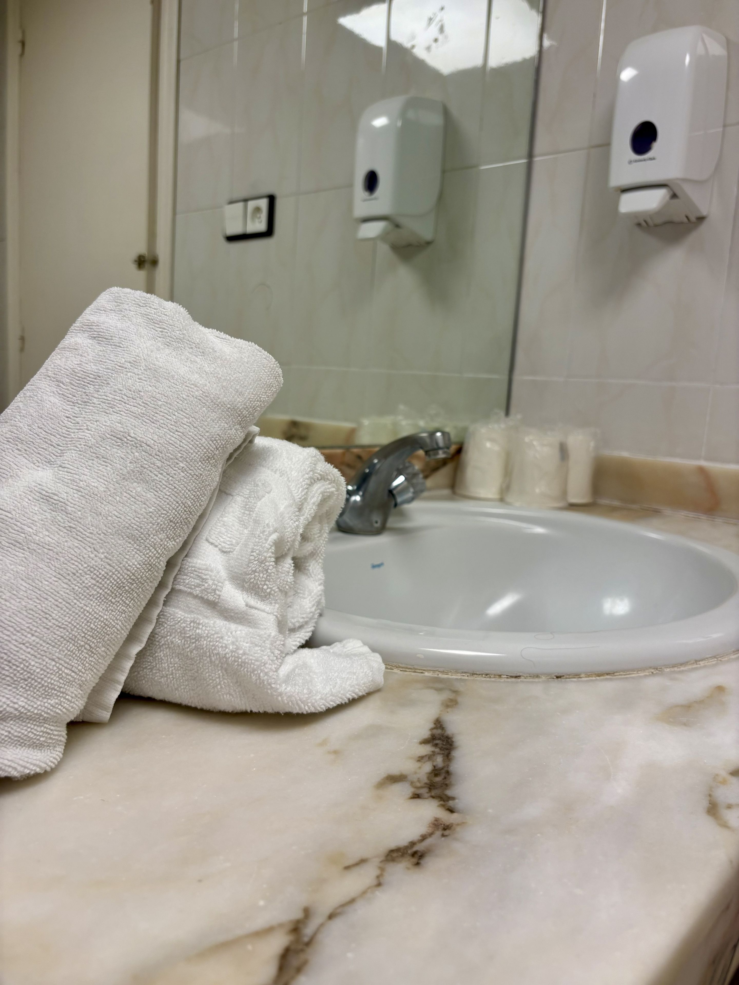 Baño con lavamanos de mármol, una toalla y dispensador de jabón.