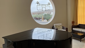 Une pièce comprenant un piano, un canapé, un fauteuil et une fenêtre donnant sur un bâtiment à l’extérieur.