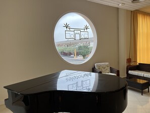 A room with a piano, a sofa, a chair, and a window with a view of a building outside.