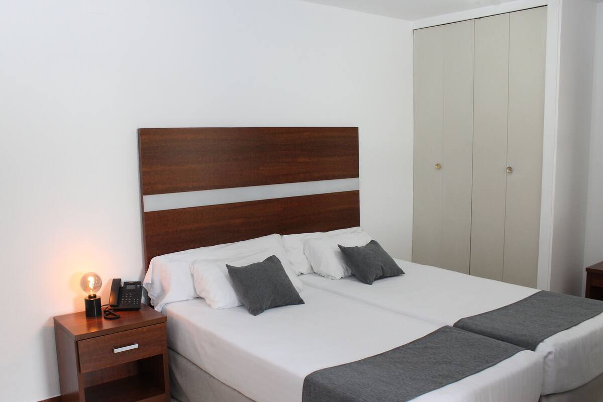 Una cama bien hecha con cabecera de madera, una mesita de noche con lámpara y un armario.