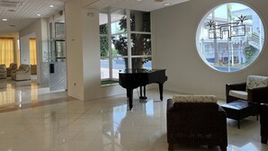 Een ruime lobby met een piano, comfortabele zitplaatsen en grote ramen met uitzicht op de straat.