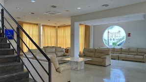 Un hall d’entrée spacieux avec un escalier, des canapés beige, une table basse en marbre et une grande fenêtre circulaire offrant une vue panoramique.