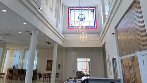 Een ruime hotel lobby met een grote kroonluchter, hoge plafonds en een centraal geplaatst glas-in-loodraam.