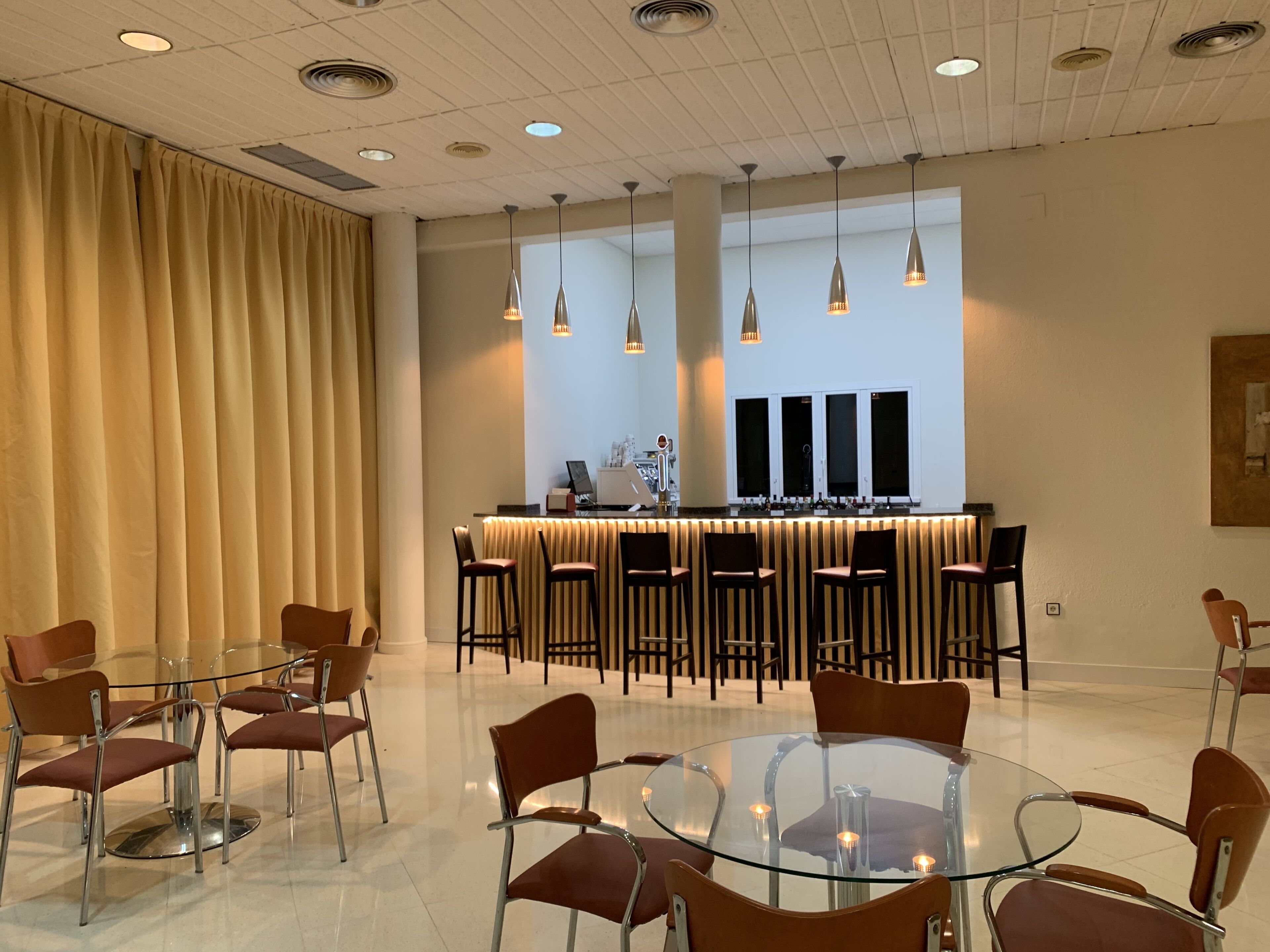 Un moderno vestíbulo de hotel con una mesa y sillas de vidrio, una recepción y lámparas colgantes.
