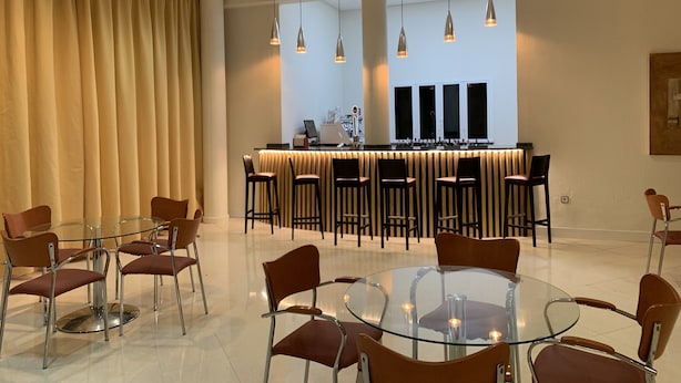 Un hall d’hôtel moderne avec une table et des chaises en verre, un comptoir d’accueil et des luminaires suspendus.